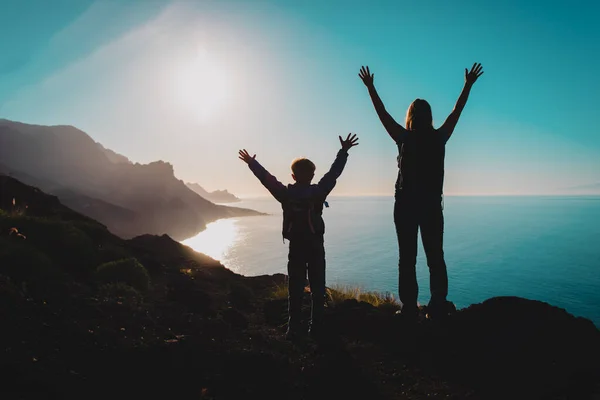 Silhueta de mãe feliz e filho viajar em montanhas pôr do sol perto do mar — Fotografia de Stock