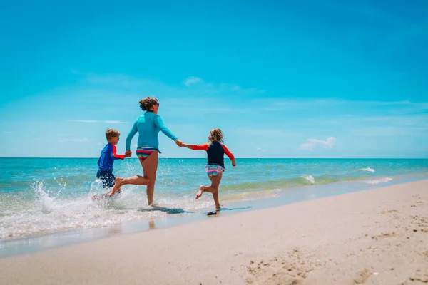 Mutter mit Kindern spielt mit Wasserlauf am Strand — Stockfoto