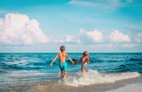 Счастливые девочка и мальчик бегут играть с волнами на пляже — стоковое фото
