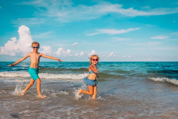 Счастливые маленькая девочка и мальчик бегают с волнами на пляже — стоковое фото