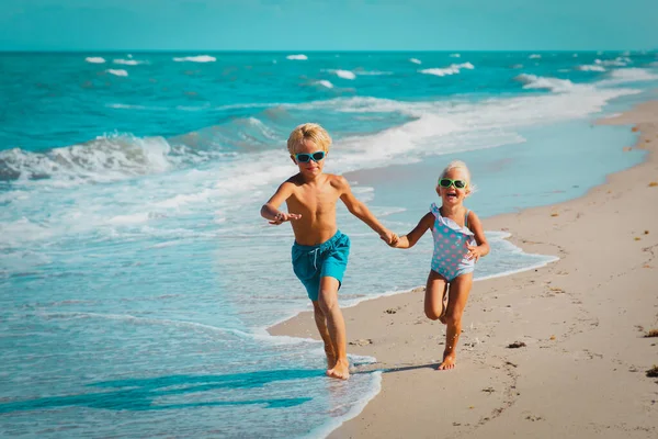 Meisje en jongen rennen op het strand, kinderen spelen met golven — Stockfoto