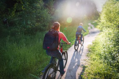Anne ve oğlu gün batımında bisiklet sürüyorlar.
