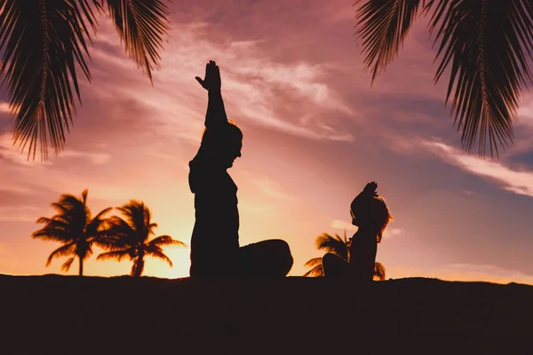 Pai e filha silhuetas exercício no pôr do sol praia, família fazendo ioga — Fotografia de Stock