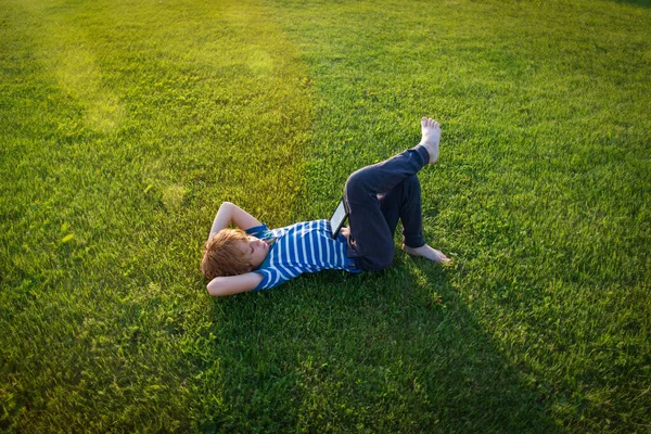 Pojke läsa bok om gräs, unge sommar lärande — Stockfoto