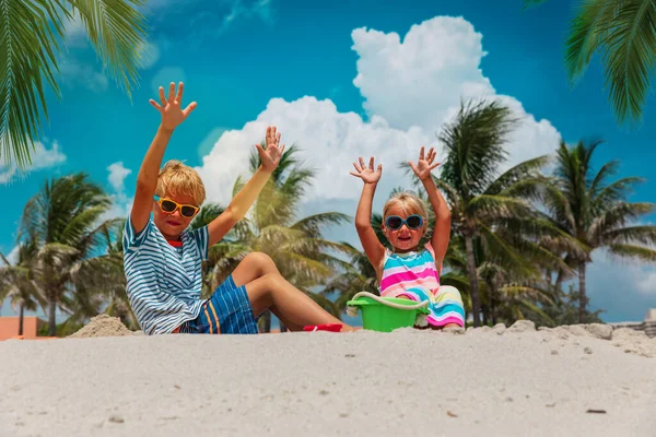 Niños alegres- niño y niña juegan con arena en la playa con palmeras — Foto de Stock