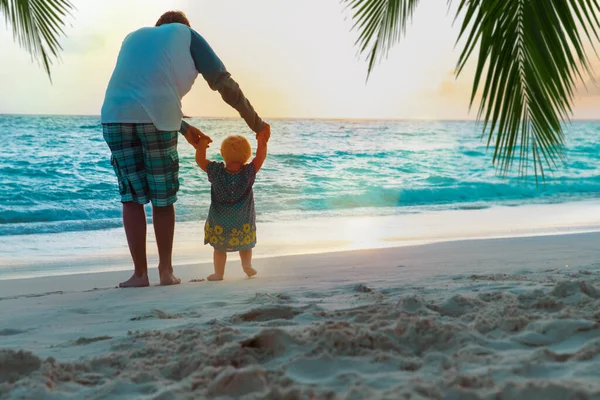 Otec a malá dcera dělat první kroky na pláži západ slunce — Stock fotografie