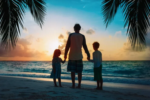 Pai e crianças andando na praia ao pôr do sol — Fotografia de Stock