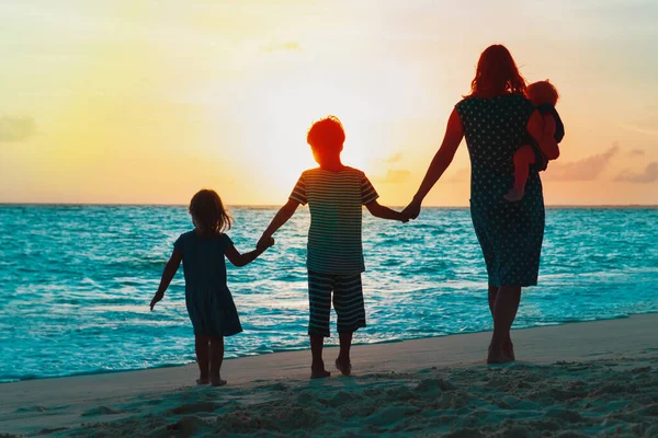 Moeder met kinderen wandelen op het strand bij zonsondergang — Stockfoto