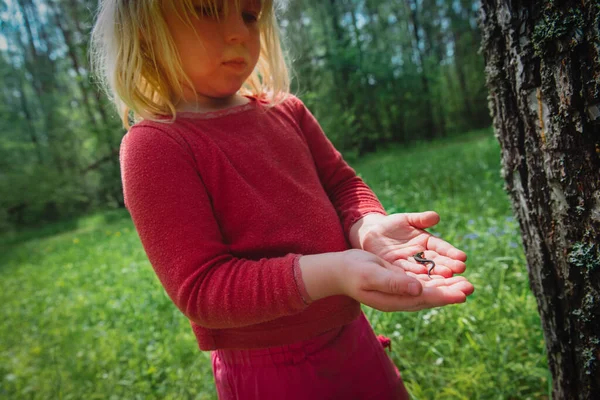 Menina segurando e olhando para lagarto na natureza — Fotografia de Stock