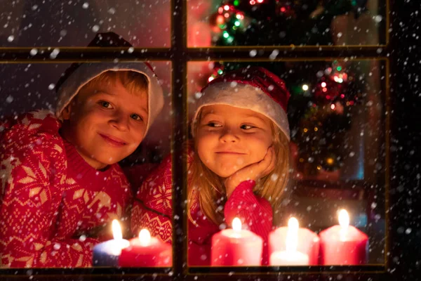 Αγόρι και κορίτσι κοιτάζοντας κεριά Χριστουγέννων δει από το εξωτερικό παράθυρο — Φωτογραφία Αρχείου