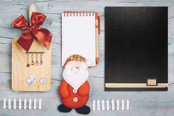 Christmas menu background with notebook and empty blackboard, kitchen utensils doll Santa Claus and ornaments