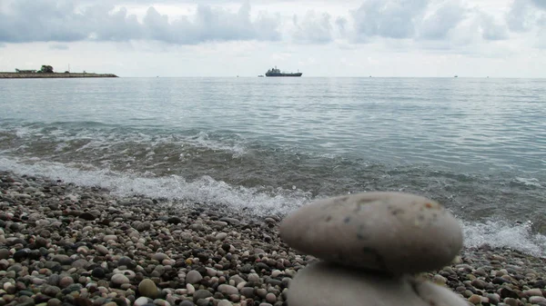 a pile of stones on the beach, the silhouette of a ship is visible on the horizon