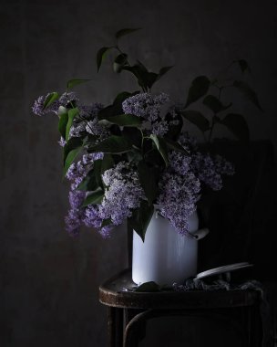 Eski bir sandalyenin üzerinde, arka plandaki karanlık bir odanın ön manzarasında, bahar (yaz) demetinde bir demet leylakla hayat.