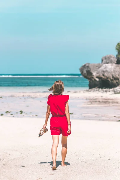 裸足で海岸を歩く赤いドレスの女の子。トロピカルなビーチ、バリ島。晴れた日. — ストック写真