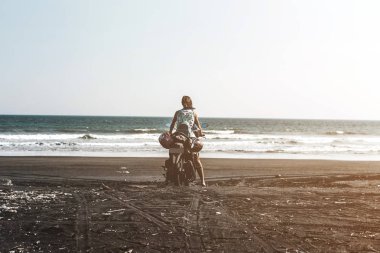 Genç kadın siyah kum Plajı'nda bir scooter sürme. Bali Adası.