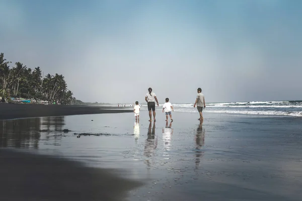 BALI, INDONÉSIE - 19 MAI 2018 : Deux pères et 2 fils sur la plage de sable noir . — Photo