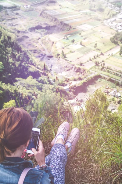 Successful woman hiker using smartphone at cliff edge on mountain top. Bali island.