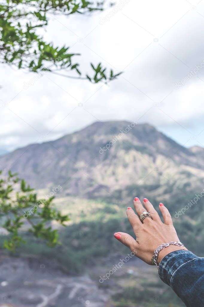 Woman hand on mountain background. Volcano Batur. Bali island.