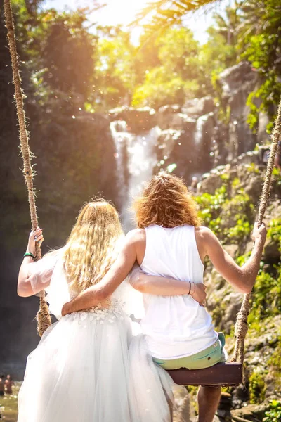 Young honeymoon couple swings in the jungle near the lake, Bali island, Indonesia.