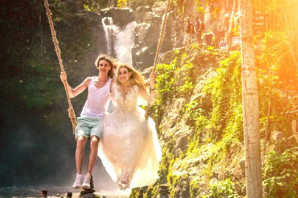 Young honeymoon couple swings in the jungle near the lake, Bali island, Indonesia.