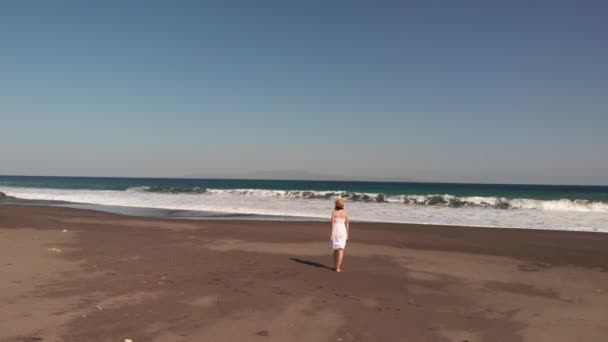 4k antenn flygande footage av ung kvinna i vit klänning promenerar på svarta vulkaniska stranden, ön Bali. — Stockvideo