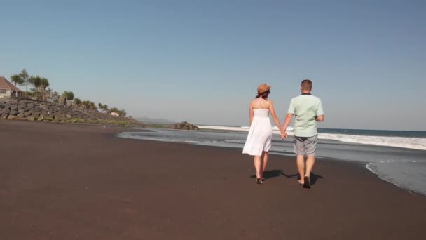 4k antenn flyger video av ungt par på stranden med svart vulkansand på solnedgång. Ön Bali. — Stockvideo