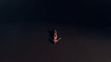 4 k hava üst siyah volkanik kum ile sahilde bikinili genç kadının uçan video görüntüleyin. Bali Adası.