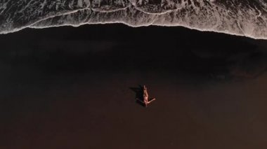 4 k hava üst siyah volkanik kum ile sahilde bikinili genç kadının uçan video görüntüleyin. Bali Adası.