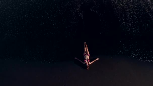 4 k antenne boven vliegende video van jonge vrouw in bikini op het strand met zwart vulkanisch zand bekijken. Bali eiland. — Stockvideo