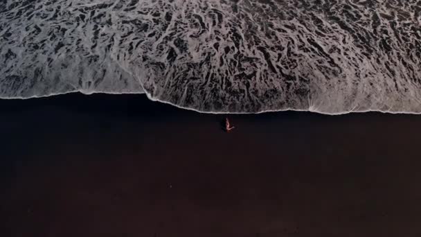 4K vista aérea superior vídeo voador de mulher jovem em biquíni na praia com areia vulcânica preta. Ilha de Bali . — Vídeo de Stock