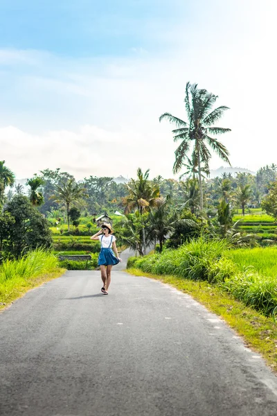 Retrato tropical de una joven mujer feliz con sombrero de paja en un camino con cocoteros y árboles tropicales. Isla de Bali . — Foto de Stock