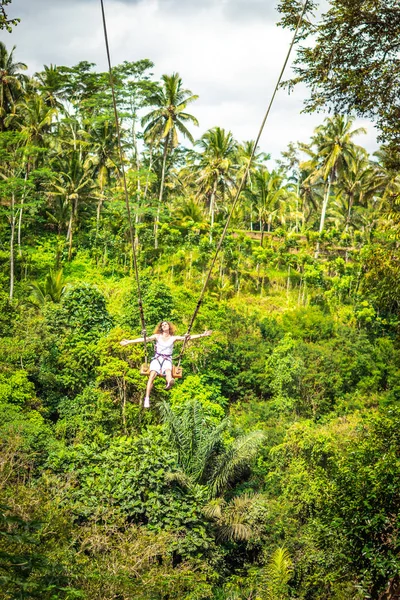 Joven turista con el pelo largo balanceándose en el acantilado en la selva de una isla tropical de Bali . — Foto de Stock