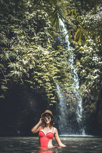 Jonge vrouw toeristische met stro hoed in de diepe jungle met waterval. Echte avontuur concept. Bali eiland. — Stockfoto