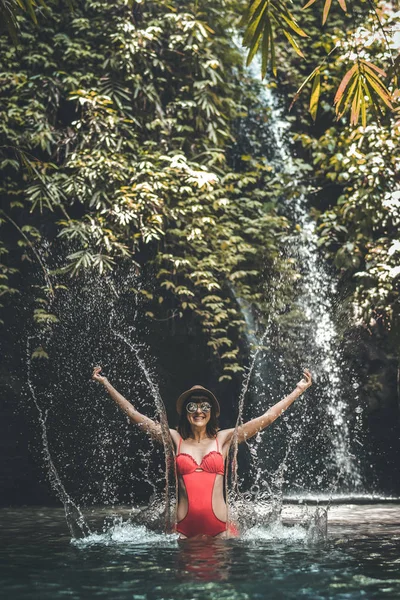 Gelukkig jonge vrouw toeristische met stro hoed in de diepe jungle met waterval. Echte avontuur concept. Bali eiland. — Stockfoto