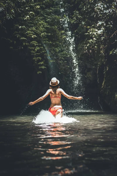 Hátulnézet fiatal nő turisztikai fut a folyó, vízesés mély dzsungelben. Igazi kaland fogalma. Bali szigetén. — Stock Fotó