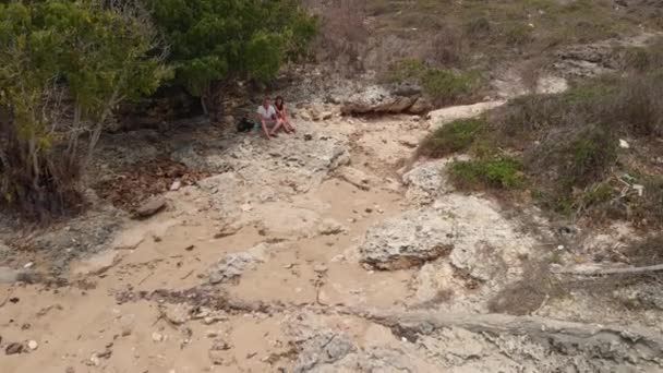 4K vuelo aéreo drone video de jóvenes turistas en pareja en la playa rocosa salvaje. Isla de Bali . — Vídeos de Stock