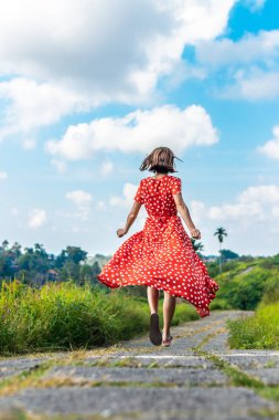 Genç kadın turist lon kırmızı elbise rainforest iz üzerinde çalışan. Bali Adası.