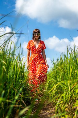 Kırmızı elbiseli bir iz ile uzun yeşil çim üzerinde yürüyen genç bir kadın. Bali Adası.