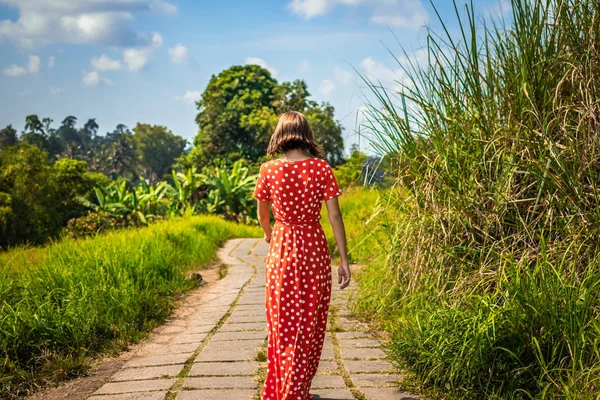 Jonge vrouw toerist in een lon rode jurk lopen op de trail regenwoud. Bali eiland. — Stockfoto