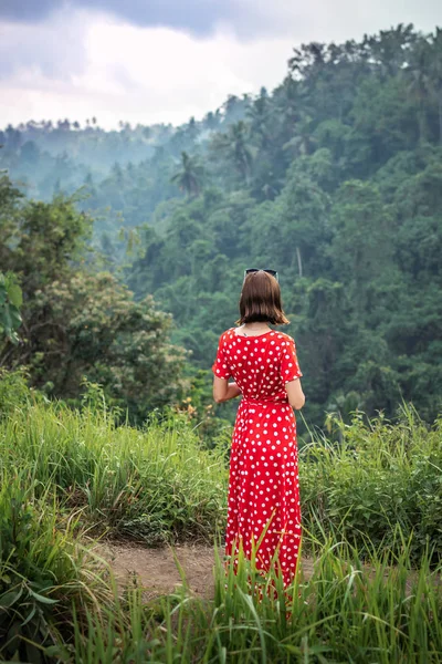 Mujer joven turista en un vestido rojo lon caminando por el sendero de la selva tropical. Isla de Bali . — Foto de Stock