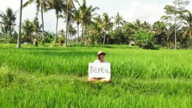 Açık havada beyaz tahta ve el yazısı söz tropikal olan kadın. Görüntüleri uçan uçak. Yeşil parlak tropikal arka plan. Güzel tropikal seyahat kavramı. Bali.