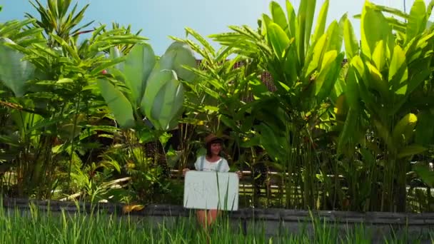 Młoda kobieta trzyma tablicę z podróży tekst. Podróżować pojęcie, latanie drone materiału. Zielone tło. Wyspa Bali. — Wideo stockowe