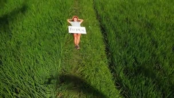 Mujer joven al aire libre con pizarra blanca y palabra de escritura tropical en ella. Imágenes voladoras de aviones no tripulados. Fondo tropical brillante verde. Hermoso concepto de viaje tropical. Isla de Bali . — Vídeos de Stock