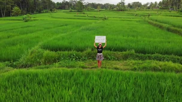 Bonne année 2019. Vidéo de drone volant 4K de jeune femme avec chapeau de Père Noël et tableau blanc avec texte manuscrit posant parmi les rizières vertes sur l'île de Bali . — Video