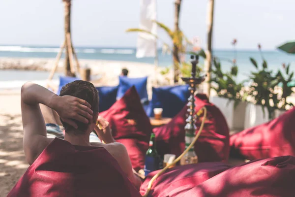 Man roken Shisha op kant een strandrestaurant naast de zee. Shisha roken. Bali eiland. — Stockfoto