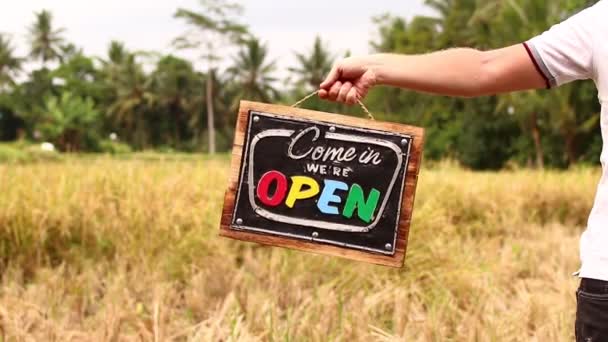 Offene Schildertafel in der Hand eines Mannes vor tropischem Hintergrund. geschossen auf bali island, full hd. — Stockvideo