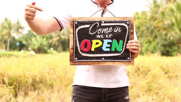 Open sign styrelsen i en man händerna på en tropisk natur bakgrund. Shooted på ön Bali, full Hd. — Stockvideo