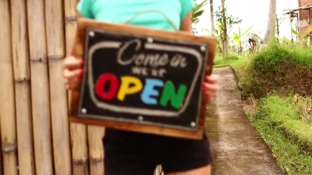 Offene Schildertafel in der Hand einer Frau vor tropischem Hintergrund. geschossen auf bali island, full hd. — Stockvideo