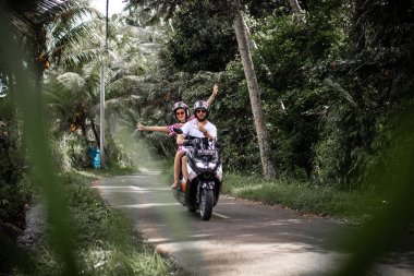 BALI, INDONESIA - DECEMBER 26, 2018: Young couple riding scooter in the rainforest, Bali island.