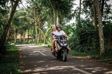 BALI, INDONESIA - DECEMBER 26, 2018: Young couple riding scooter in the rainforest, Bali island.
